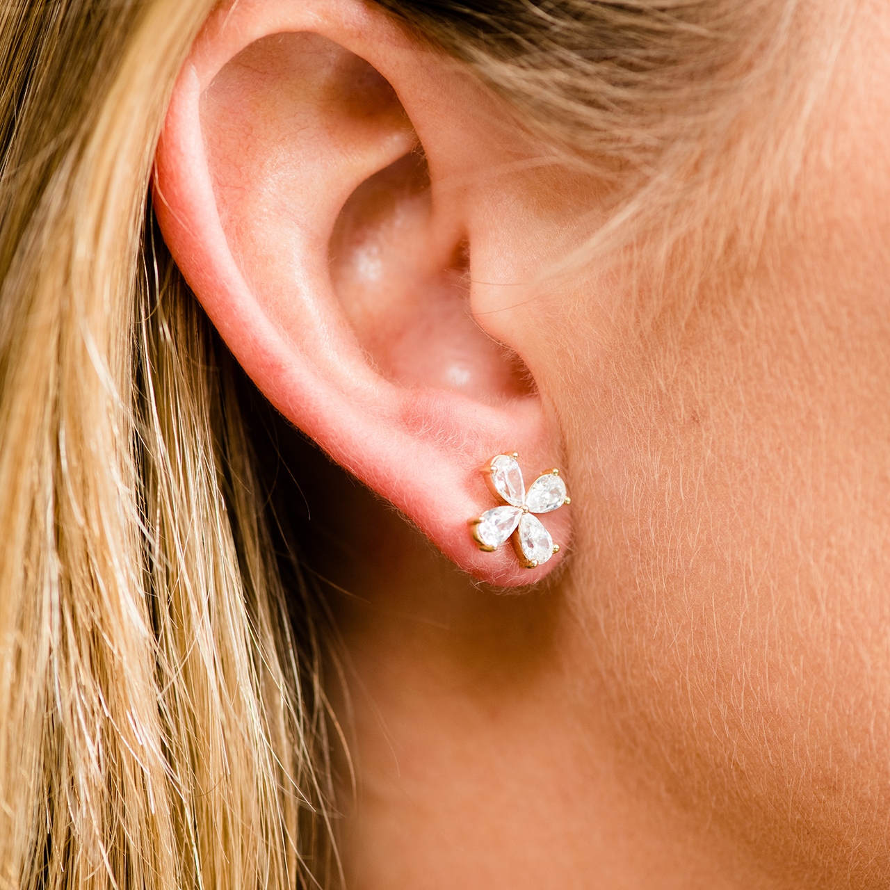Close-up of a gold flower stud earring with four pear-cut diamond petals worn on an ear.