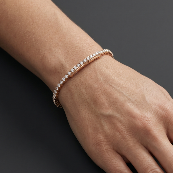 Close-up lifestyle view of a classic 14k rose gold tennis bracelet featuring a continuous, uniform row of brilliant round-cut diamonds styled on a wrist.