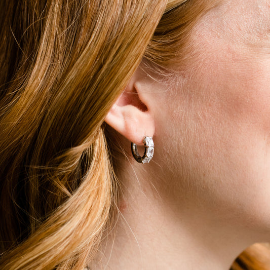 A pair of 14K white gold huggie hoops, shown from a side angle, highlighting the stacked diamonds and hinged closure on ear.