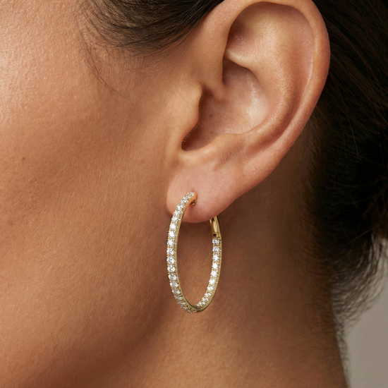 A pair of 14K yellow gold large hoop earrings, shown from a side angle, highlighting the line of diamonds and the hinged closure on hand.