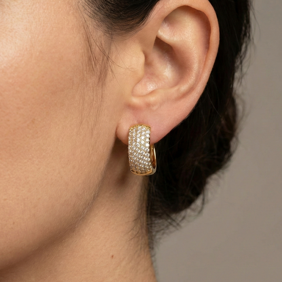 A pair of 14K yellow gold chunky huggie hoops with the entire front surface covered in pavé diamonds, shown from the front on ear.