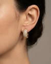 A pair of 14K yellow gold chunky huggie hoops with the entire front surface covered in pavé diamonds, shown from the front on ear.