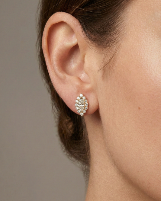 A pair of 14K yellow gold stud earrings with a marquise-shaped cluster of diamonds and a halo, shown from the front on ear.