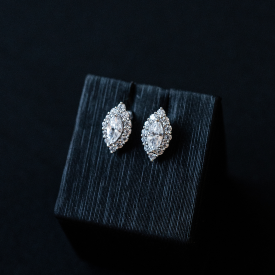 White gold Amorati Enchanted Marquise Stud Earrings displayed on top of a textured black jewelry box against a dark background.