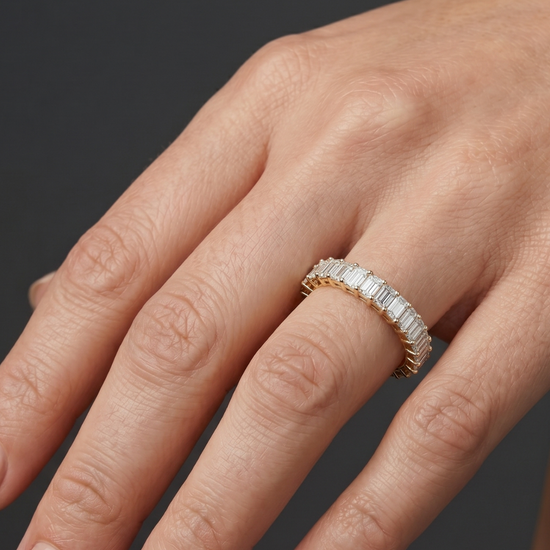 Lifestyle view of a model wearing a luxurious 14k yellow gold eternity ring fully set with a continuous row of shimmering emerald-cut diamonds.