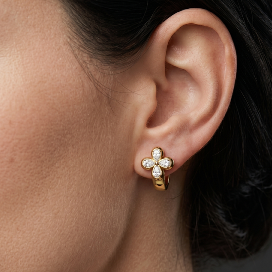 Close-up lifestyle view of a 14k yellow gold huggie earring featuring a prominent clover-shaped four-leaf flower motif studded with pear-cut white diamonds.
