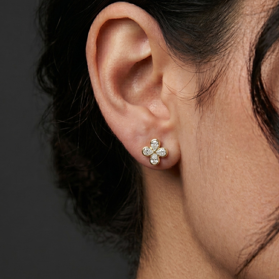 Close-up profile view of a 14k yellow gold stud earring shaped like a four-leaf clover flower, set with four shimmering pear-cut diamonds.