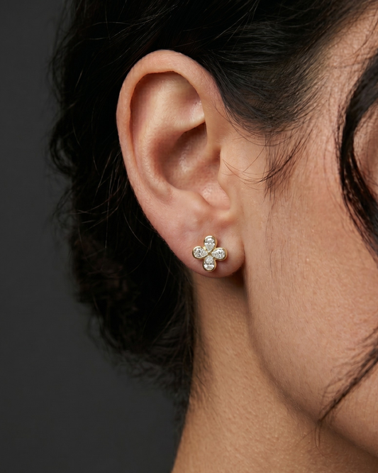 Close-up profile view of a 14k yellow gold stud earring shaped like a four-leaf clover flower, set with four shimmering pear-cut diamonds.