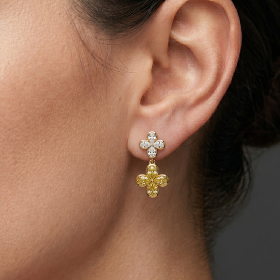 Lifestyle view of a model wearing 14k yellow gold two-tone clover drop earrings featuring a white diamond four-leaf top stud and a dangling yellow diamond clover drop.