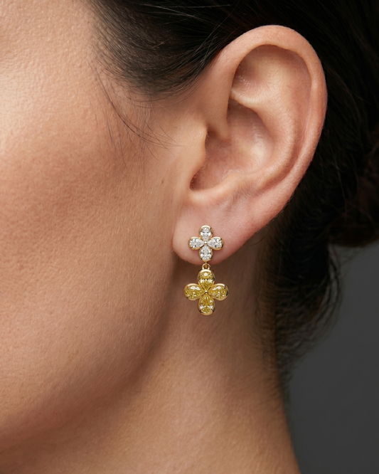 Lifestyle view of a model wearing 14k yellow gold two-tone clover drop earrings featuring a white diamond four-leaf top stud and a dangling yellow diamond clover drop.
