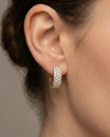 A pair of 14K yellow gold huggie hoops with three parallel rows of pavé diamonds, shown from the front on ear.