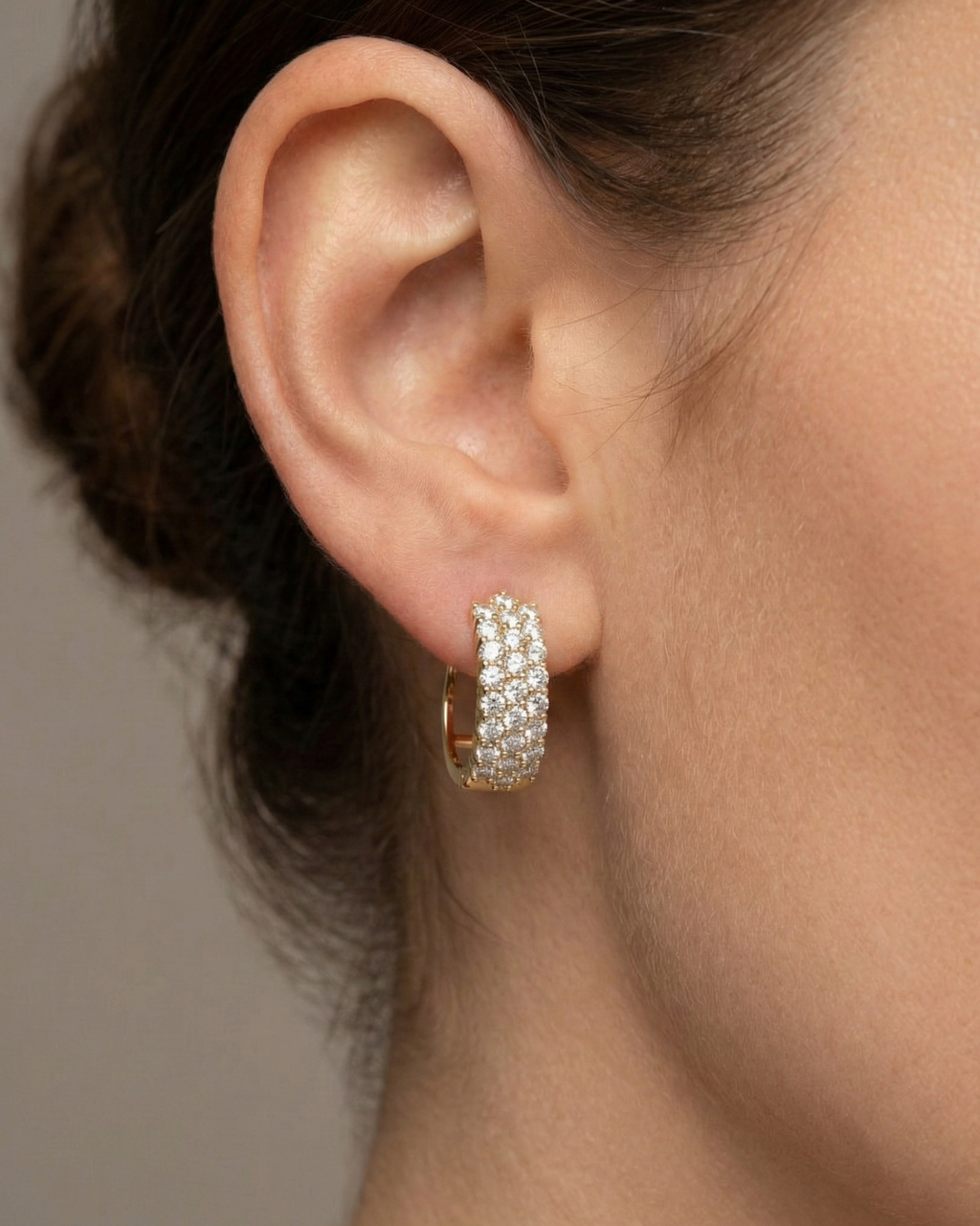 A pair of 14K yellow gold huggie hoops with three parallel rows of pavé diamonds, shown from the front on ear.