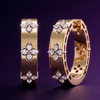 Close-up of Amorati yellow gold huggie earrings featuring diamond clover designs against a dark purple background.