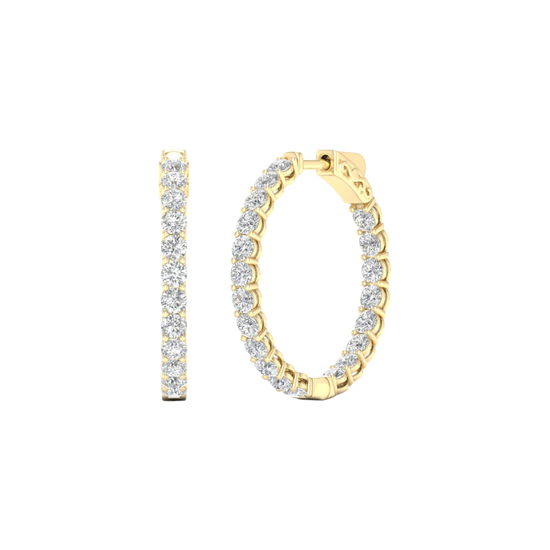 A close-up of a pair of 14K yellow gold huggie hoop earrings with a continuous line of brilliant round-cut diamonds, shown on a black background to highlight their sparkle.