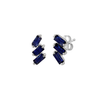 A pair of cascading stud earrings featuring a vertical arrangement of three baguette-cut blue sapphires. The rectangular gemstones are staggered in a step-like formation and held in a minimalist 18k white gold setting, shown against a clean, white studio background.