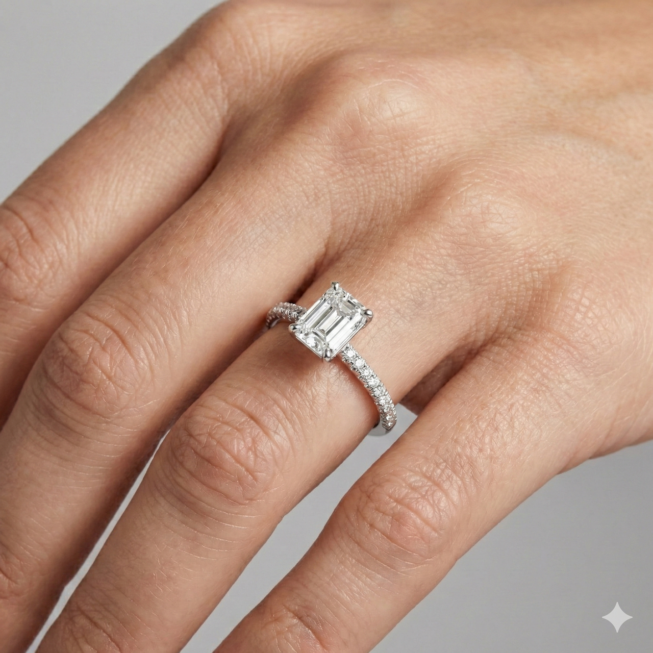 Emerald cut diamond engagement ring in 14k white gold with a pavé diamond band and cathedral setting on a hand.