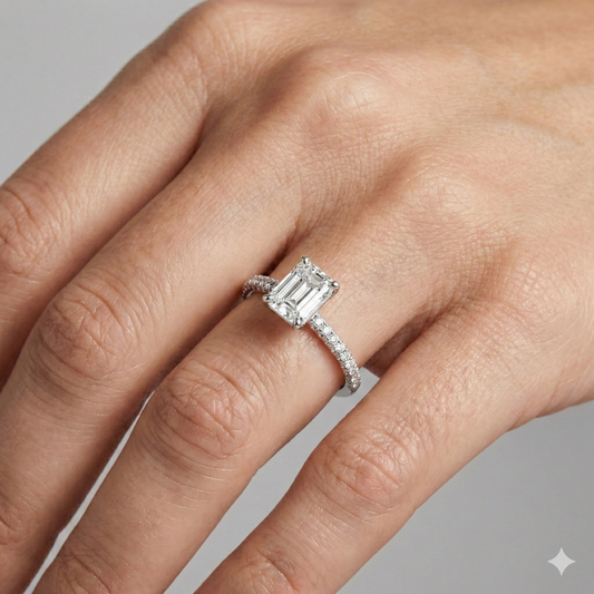 Emerald cut diamond engagement ring in 14k white gold with a pavé diamond band and cathedral setting on a hand.