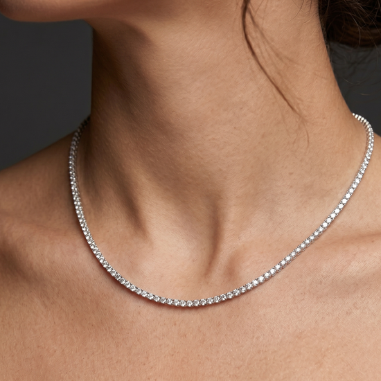 Lifestyle view of a model wearing a classic white gold or platinum tennis necklace featuring a continuous uniform strand of brilliant round-cut diamonds.