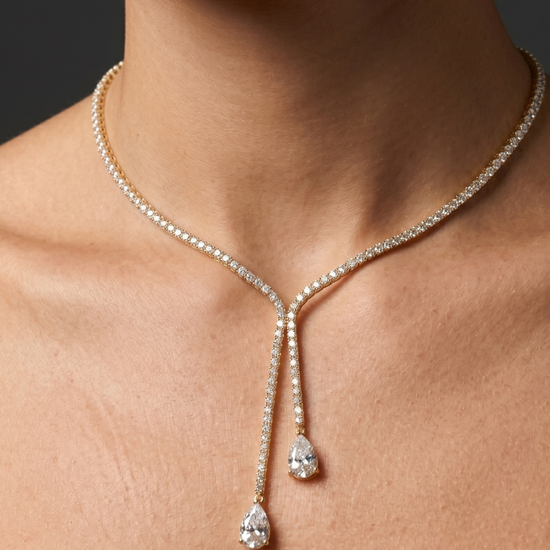 Lifestyle view of a model wearing an elegant 14k yellow gold diamond lariat tennis necklace featuring asymmetric dangling pear-cut diamond drops.
