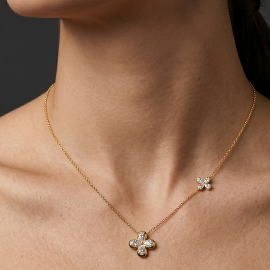 Lifestyle view of a model wearing a 14k yellow gold station necklace featuring a central four-leaf clover diamond pendant and a smaller clover accent station along the chain.