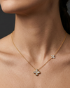 Lifestyle view of a model wearing a 14k yellow gold station necklace featuring a central four-leaf clover diamond pendant and a smaller clover accent station along the chain.