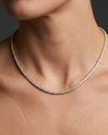 Lifestyle view of a model wearing a delicate 14k yellow gold tennis necklace featuring a thin continuous uniform strand of round-cut white diamonds.
