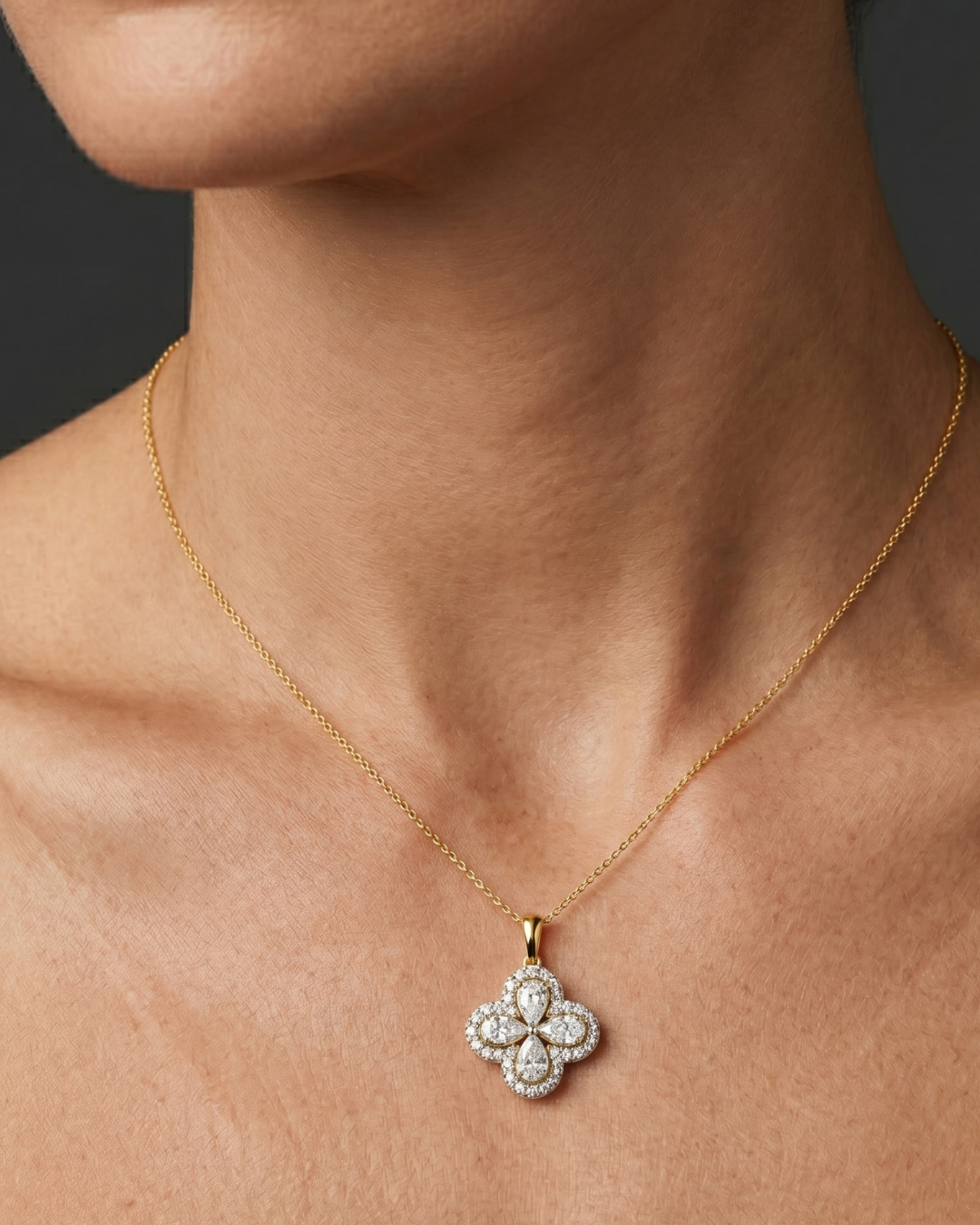 Close-up of a person's neck and collarbone wearing a fine gold chain necklace with a diamond flower pendant featuring pear-shaped stones and a pavé halo.