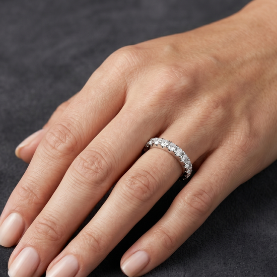 Close-up of a hand resting on a dark gray surface, wearing a white metal eternity band set with a row of round diamonds.