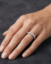 Close-up of a hand resting on a dark gray surface, wearing a white metal eternity band set with a row of round diamonds.