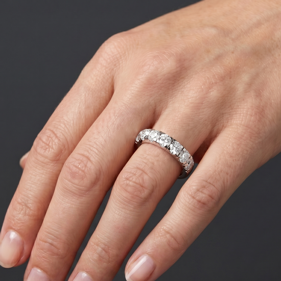 Close-up of a hand resting against a dark gray background, wearing a thick white metal band featuring a row of large, round-cut diamonds.