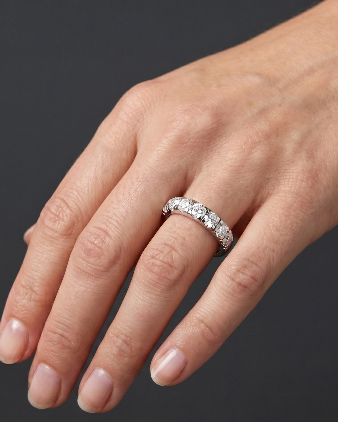 Close-up of a hand resting against a dark gray background, wearing a thick white metal band featuring a row of large, round-cut diamonds.