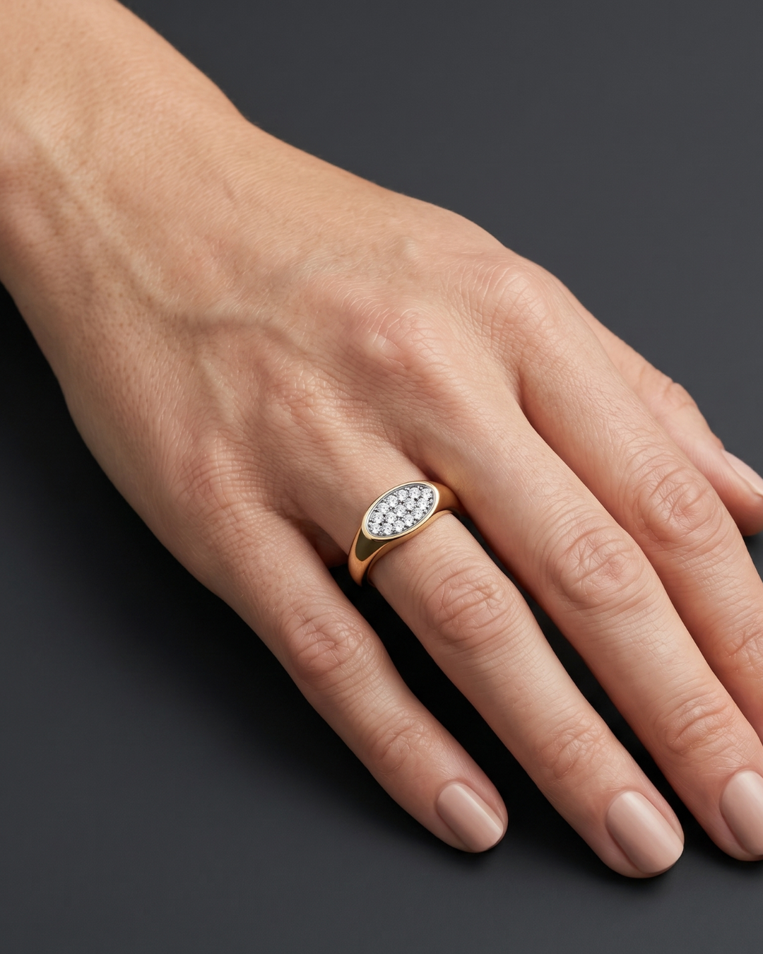 Lifestyle view of a model wearing a modern 14k yellow gold pinky signet ring featuring a flat oval face encrusted with micro-pavé white diamonds.
