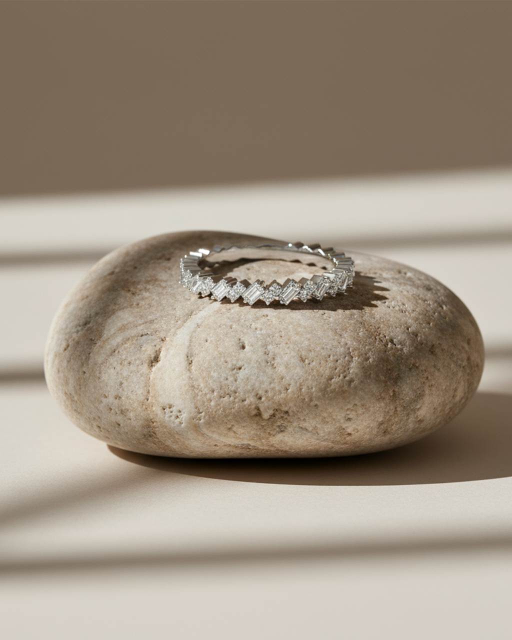 A close-up view of a 14K yellow gold band ring with an alternating pattern of baguette and round diamonds on a beige stone.