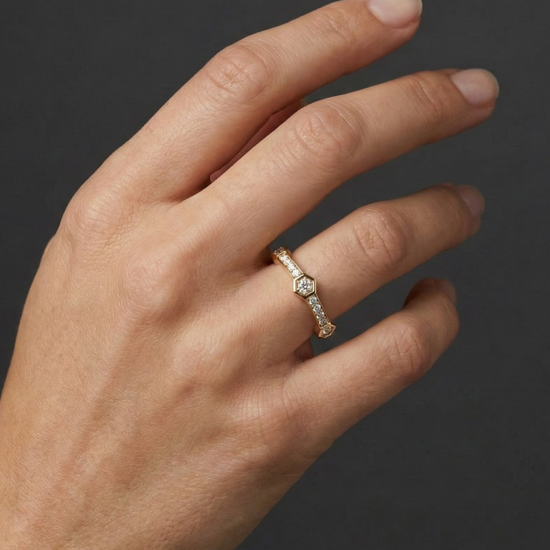 Close-up of a hand wearing a delicate 14k yellow gold diamond ring, featuring a small round center diamond accented by pavé-set diamonds along a slim band, photographed against a dark background to highlight subtle sparkle and refined elegance.