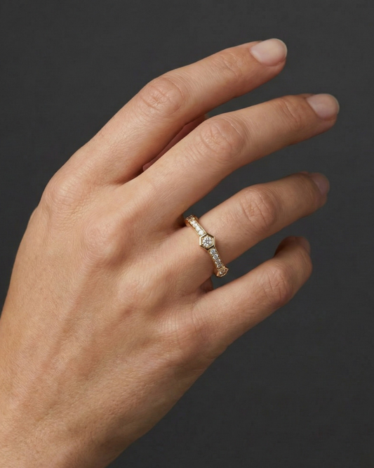 Close-up of a hand wearing a delicate 14k yellow gold diamond ring, featuring a small round center diamond accented by pavé-set diamonds along a slim band, photographed against a dark background to highlight subtle sparkle and refined elegance.