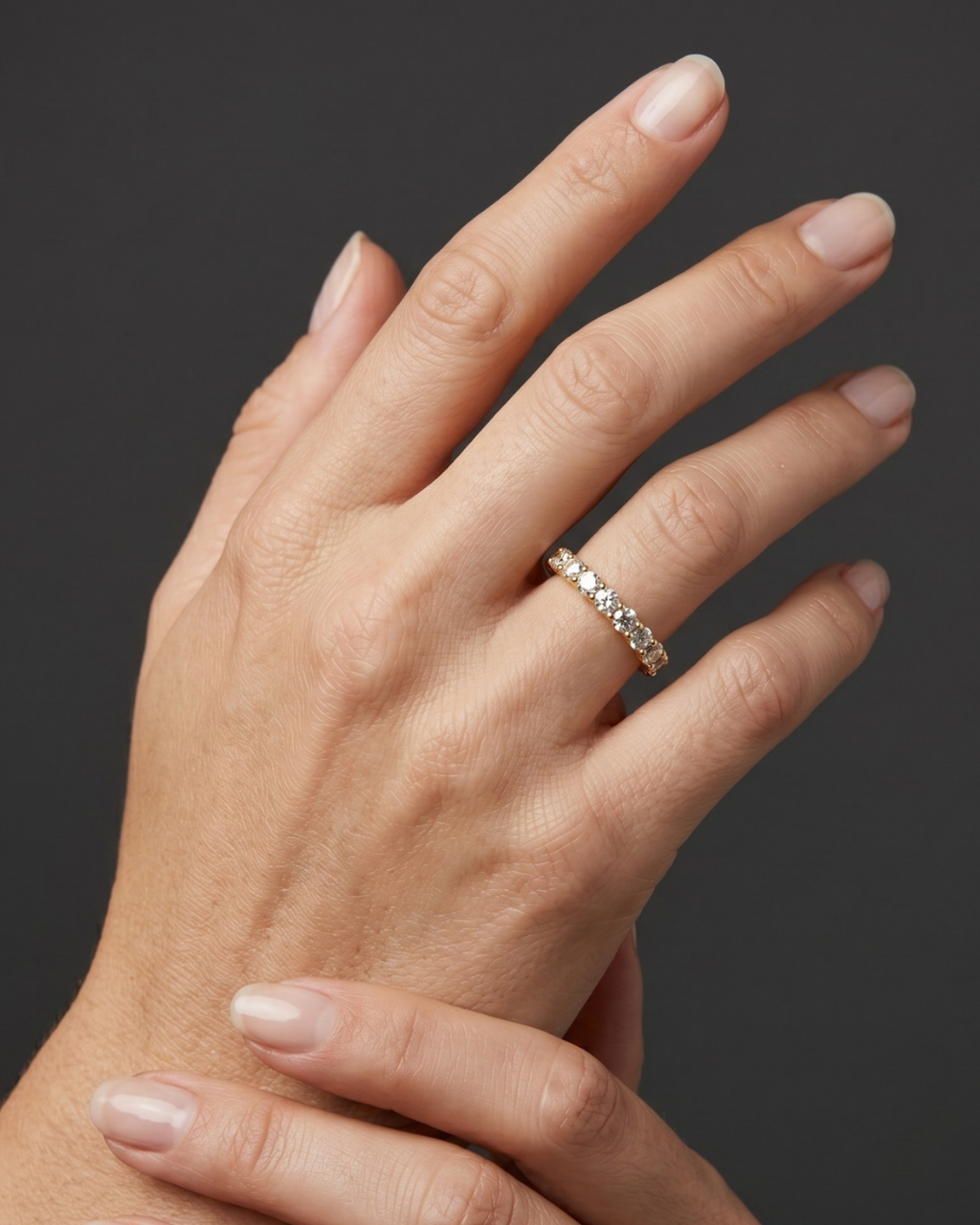 Close-up of a woman's hand wearing a yellow gold diamond eternity band against a dark gray background.