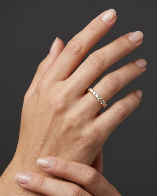 Close-up of a woman's hand wearing a yellow gold diamond eternity band against a dark gray background.