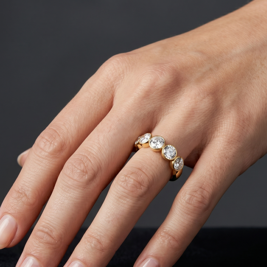 Close-up of a hand resting on a black surface, wearing a thick gold band featuring a row of five round, bezel-set diamonds.