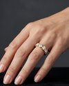 Close-up of a hand resting on a black surface, wearing a thick gold band featuring a row of five round, bezel-set diamonds.