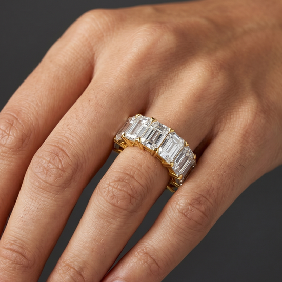 Lifestyle view of a model wearing a heavy-carat 14k yellow gold eternity ring featuring exceptionally large, vertically set emerald-cut diamonds.