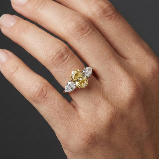 Close-up hand view of a 3.20 Cttw. Soleil Oval Canary Yellow and White Diamond Trilogy Engagement Ring, featuring a 2-carat Vivid Canary center stone and two 0.60ct white diamond side stones set in 14K gold.