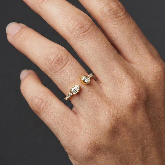 Close-up of a hand wearing a delicate yellow gold diamond ring, featuring pear-cut diamonds set on a slim pavé band, photographed against a dark background to highlight refined sparkle and elegant everyday styling.