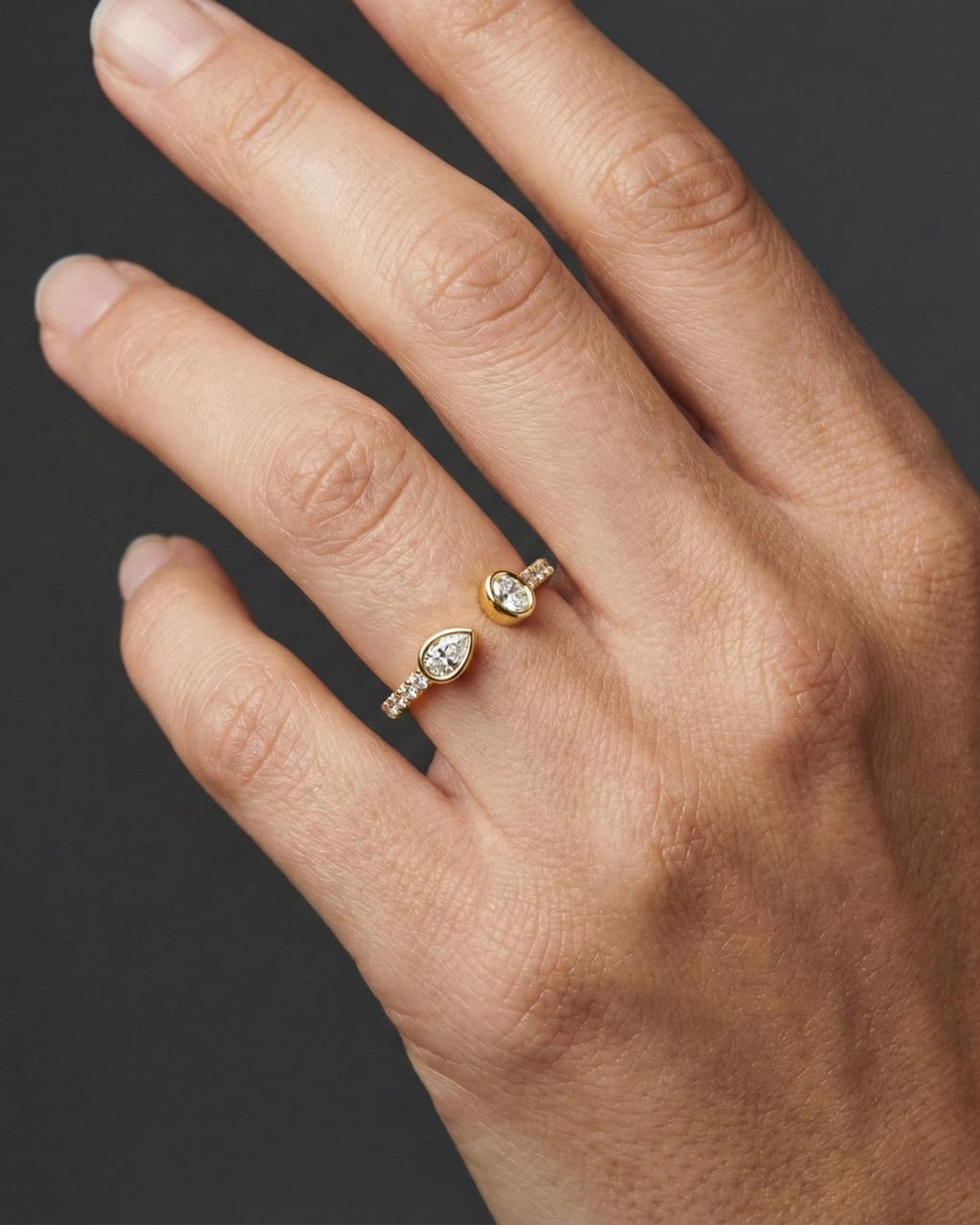 Close-up of a hand wearing a delicate yellow gold diamond ring, featuring pear-cut diamonds set on a slim pavé band, photographed against a dark background to highlight refined sparkle and elegant everyday styling.