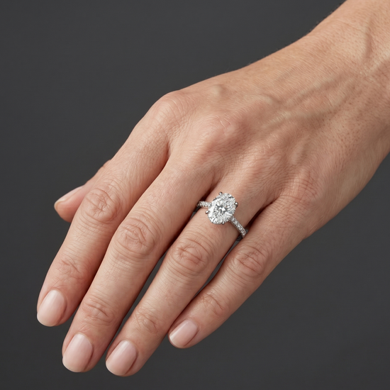 Elegant white gold engagement ring featuring a large oval-cut center diamond and a pavé diamond band, worn on a woman's hand.