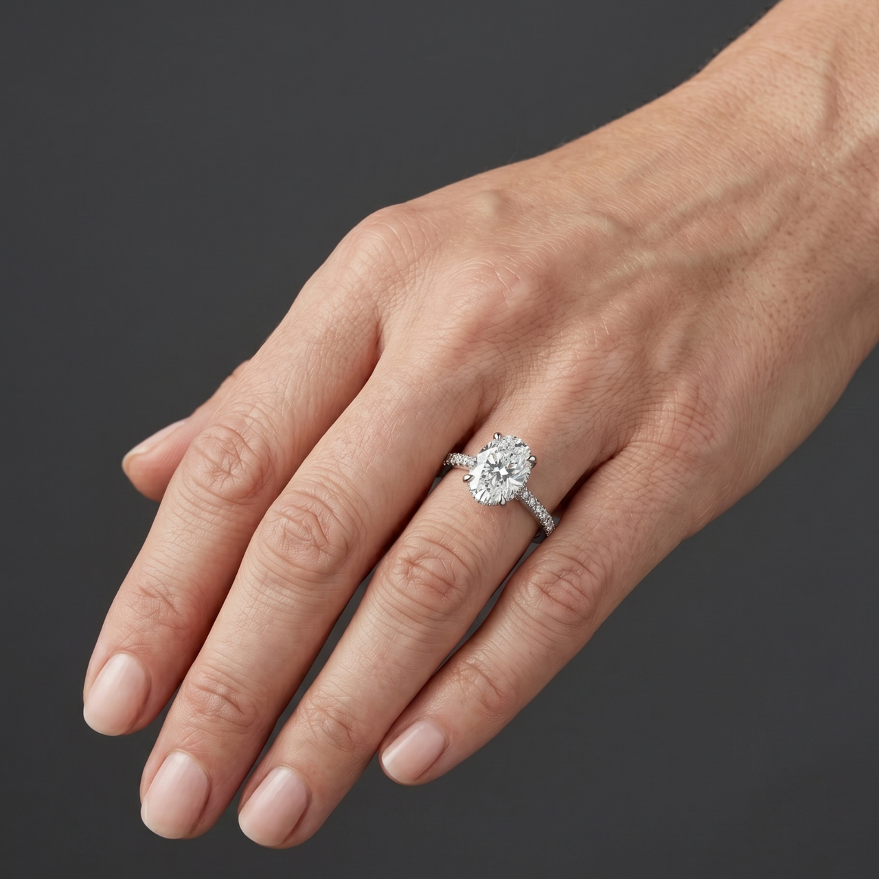 Elegant white gold engagement ring featuring a large oval-cut center diamond and a pavé diamond band, worn on a woman's hand.
