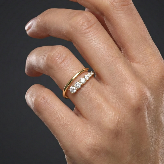 Close-up of a hand wearing a 14k yellow gold diamond band featuring a row of round brilliant-cut diamonds set across a slim polished band, photographed against a dark background to highlight delicate sparkle and timeless elegance.