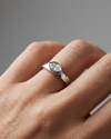 A top-down view of a 14K white gold bypass ring with a single, horizontally-set oval diamond in a bezel setting on hand.