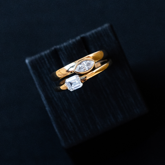 Yellow gold Amorati whispering signet ring featuring marquise and emerald cut diamonds, resting on a black textured display block.