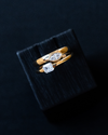 Yellow gold Amorati whispering signet ring featuring marquise and emerald cut diamonds, resting on a black textured display block.