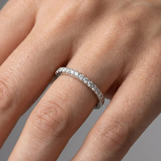 A top-down view of a 14K white gold thin band ring with a continuous line of petite, pavé-set round jewels on a finger of a hand.